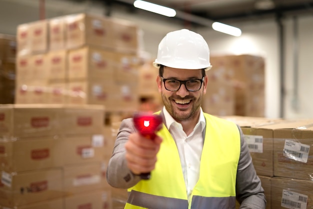 Portret van fabriek magazijnmedewerker permanent onder kartonnen dozen met streepjescodescanner laserstraal wijst naar de camera