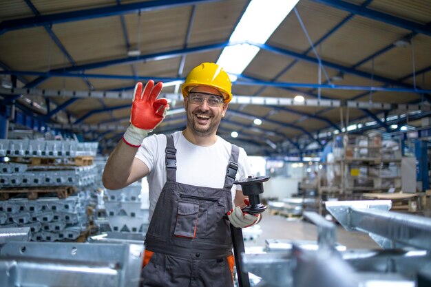 Portret van fabrieksarbeider in beschermende uitrusting houden duimen in productiehal