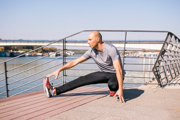 Portret van fit jonge man die zich uitstrekt been op brug in de buurt van het meer