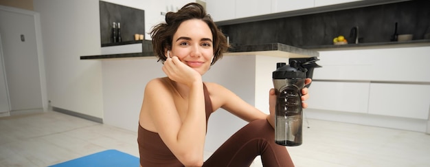 Gratis foto portret van fitnessvrouw jonge sportvrouw thuis drinkt water uit de fles na de training