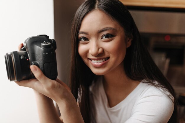 Portret van gebruind meisje met donker haar met camera in haar handen Vrouw in witte top schattige glimlach