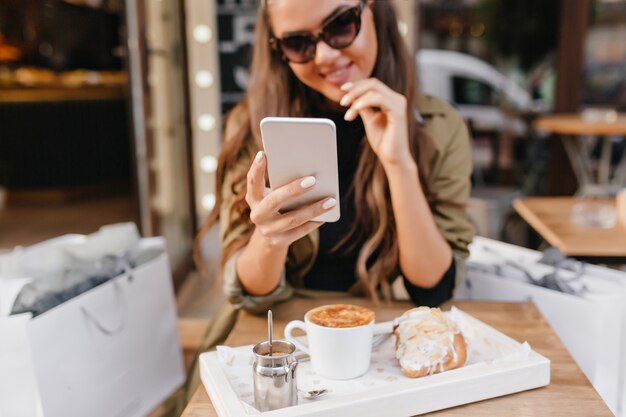 Portret van gebruinde dame met elegante manicure en kopje latte op voorgrond