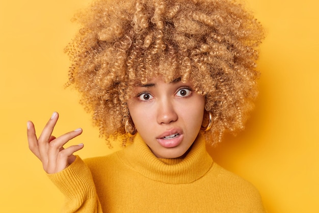 Gratis foto portret van geen idee verontwaardigde vrouw met ondervraagde uitdrukking haalt schouders op en kijkt met onzekerheid onder ogen moeilijke keuze draagt coltrui geïsoleerd over gele achtergrond. arrogant meisje