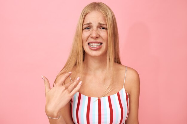 Portret van geërgerd ontevreden jonge blanke vrouw met gezicht piercing en beugels gebaar met hand op haar nek