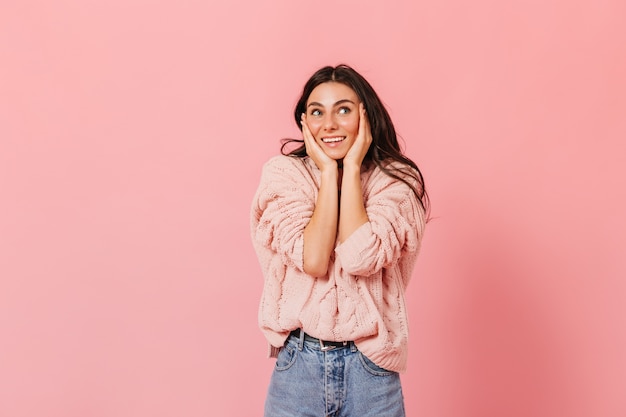 Portret van gelooid brunette meisje in roze trui in hoge geesten poseren op geïsoleerde achtergrond.