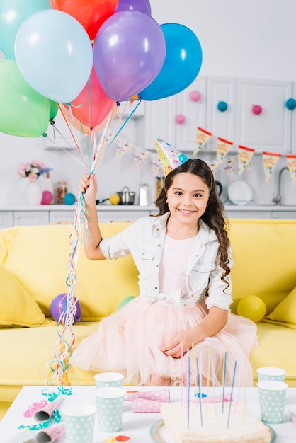 Portret van gelukkig meisje, zittend op de bank bedrijf kleurrijke ballonnen