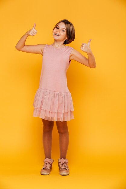 Portret van gelukkig onbezorgd meisje dat omhoog geïsoleerde duimen glimlacht toont
