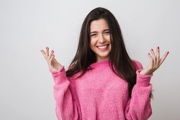 Portret van gelukkige aantrekkelijke vrouw in warme roze trui, lang haar, natuurlijke uitstraling, oprechte glimlach, positieve stemming, handen omhoog houden, zich verrast voelen, geïsoleerd