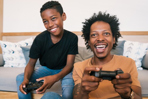 Portret van gelukkige Afro-Amerikaanse vader en zoon zittend in een banklaag en thuis console videogames samen spelen. Familie en technologieconcept.