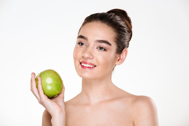 portret van gelukkige donkerbruine vrouw die groene appel houdt en weg kijkt