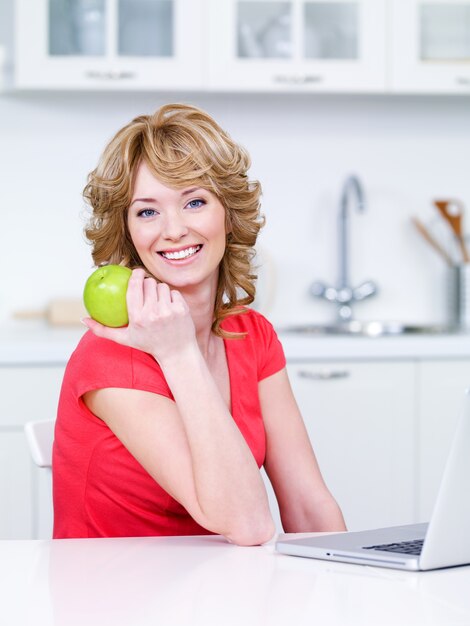 Portret van gelukkige glimlachende vrouw met groene appelzitting in de keuken
