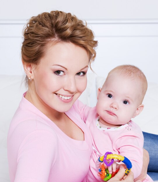 Portret van gelukkige jonge attactive moeder die met haar baby thuis op het bed ligt