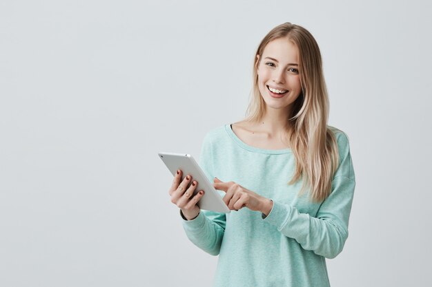 Portret van gelukkige jonge blonde bedrijfsvrouw in vrijetijdskleding die tablet gebruiken