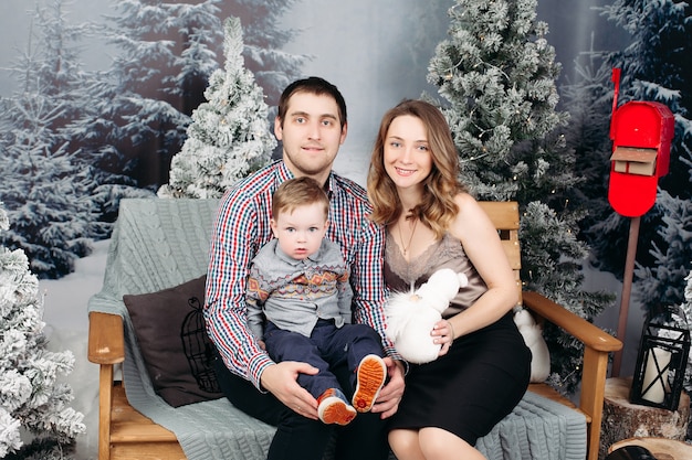 Portret van gelukkige jonge familie samen zitten op de bank tijdens kerst in de studio, poseren, glimlachen en kijken naar de voorkant