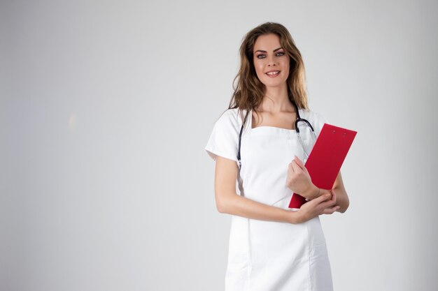 Portret van gelukkige jonge lachende vrouwelijke arts die een medische platenbord bevat.