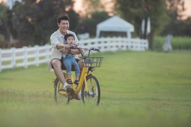 Portret van gelukkige jonge vader en zoon op een fiets. vader en zoon spelen in het park bij zonsondergang. mensen die plezier hebben op het veld. concept van vriendelijke familie en zomervakantie.