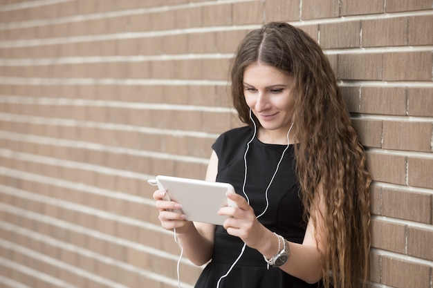 Portret van gelukkige jonge vrouw luisteren naar muziek op tablet op de straat