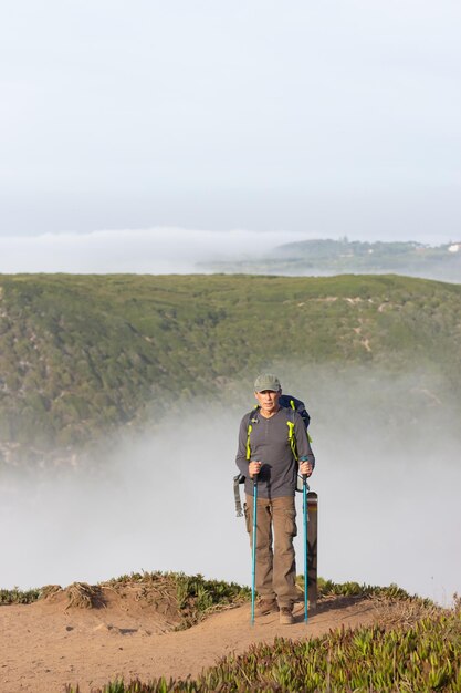Portret van gelukkige mannelijke wandelaar met grijs haar. Man in vrijetijdskleding met wandelmunitie kijkend naar camera, spectaculair landschap op de achtergrond. Hobby, natuurconcept