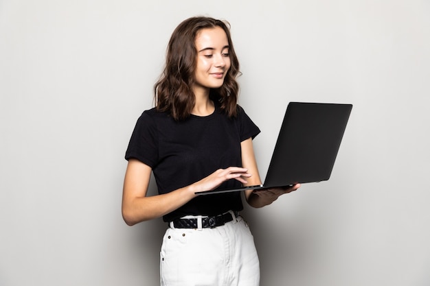 Portret van gelukkige verraste vrouw die zich met laptop bevindt die op grijze achtergrond wordt geïsoleerd