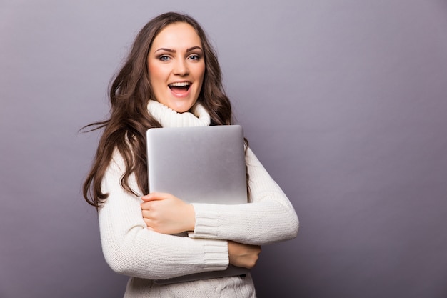 Portret van gelukkige verraste vrouw die zich met laptop bevindt die op grijze muur wordt geïsoleerd