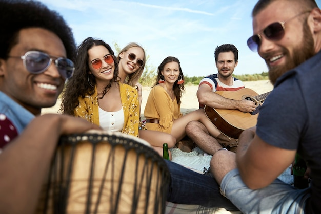 Portret van gelukkige vrienden die op het strand zitten met muziekinstrumenten