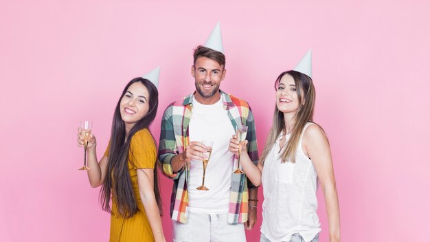 Portret van gelukkige vrienden die wijnglazen op roze achtergrond houden