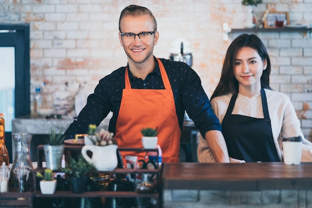 Portret van gelukkige winkelpartners die een schort dragen aantrekkelijke blanke mannelijke en vrouwelijke aziatische barista café-restauranteigenaar glimlach met zelfverzekerd en warm welkom succesvolle zakelijke plaats