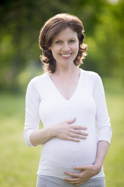 Portret van gelukkige zwangere vrouw die haar buik raakt