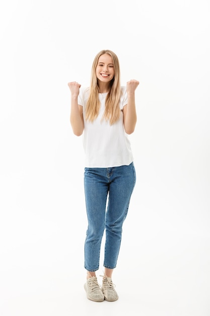 Gratis foto portret van gemiddelde lengte van een vrolijke vrouw die in wit overhemd en jeans haar succes over witte achtergrond viert.