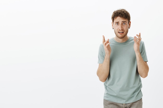 Portret van geschokt ontevreden knappe man met blond haar in trendy t-shirt, gebarend met verwarde uitdrukking, fronsen en grimassen