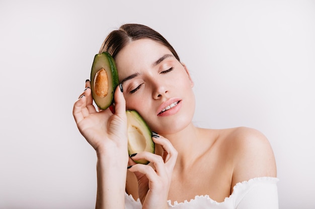 Portret van gezonde vrouw zonder make-up poseren met avocado Donkerharig model zorgt voor goede voeding