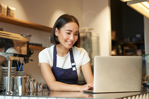 Portret van glimlachende Aziatische barista café-eigenaar ondernemer die werkt aan laptop verwerkingsorders op com