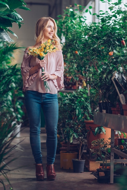 Portret van glimlachende blonde jonge vrouw die gele bloem houdt