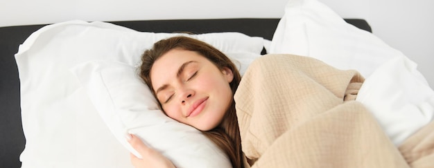 Gratis foto portret van glimlachende brunette vrouw in pyjama slapend in hotelbed ontspannend met blij gezicht