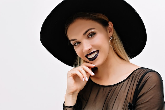 Portret van glimlachende charmante vrouw met zwarte lippenstift en zwarte hoed