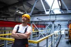 Gratis foto portret van glimlachende fabrieksarbeider met gekruiste armen staande in industriële productiehal