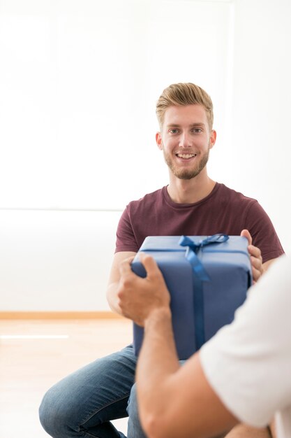 Portret van glimlachende jonge mens die giftdoos van zijn vriend neemt