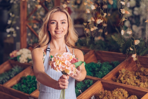 Portret van glimlachende jonge vrouwelijke bloemist die de bloemen aanbieden