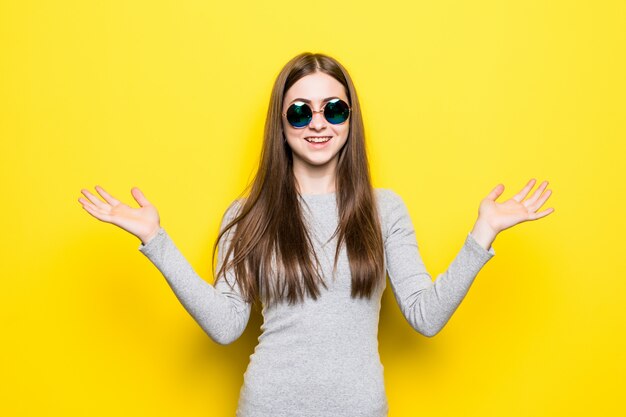 Portret van glimlachende mooie vrouw in zonnebril en kleding tegen van gele muur