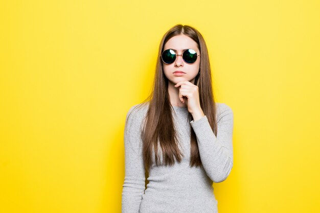 Portret van glimlachende mooie vrouw in zonnebril en kleding tegen van gele muur