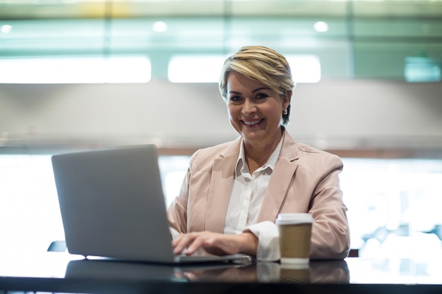 Portret van glimlachende onderneemster die laptop in wachtruimte met behulp van