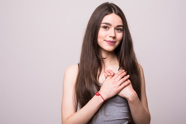 Portret van glimlachende positieve jonge vrouw houdt handen op de borst, betuigt medeleven. Vriendelijk hartelijk vriendelijk aardig meisje toont vriendelijkheid, het dragen van een leeg grijs t-shirt op een grijze muur