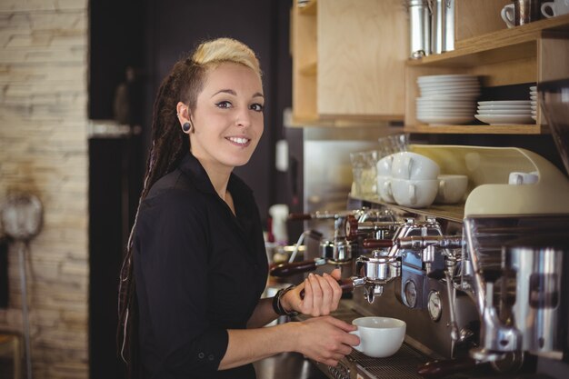 Portret van glimlachende serveerster die een kop van koffie voorbereiden