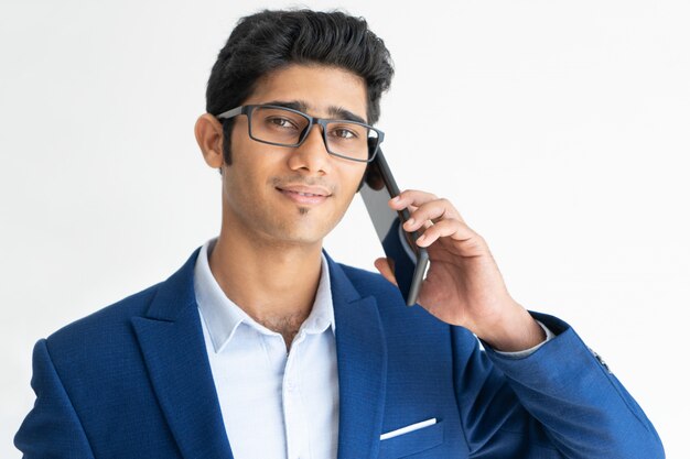 Portret van glimlachende zakenman in glazen die op smartphone spreken.