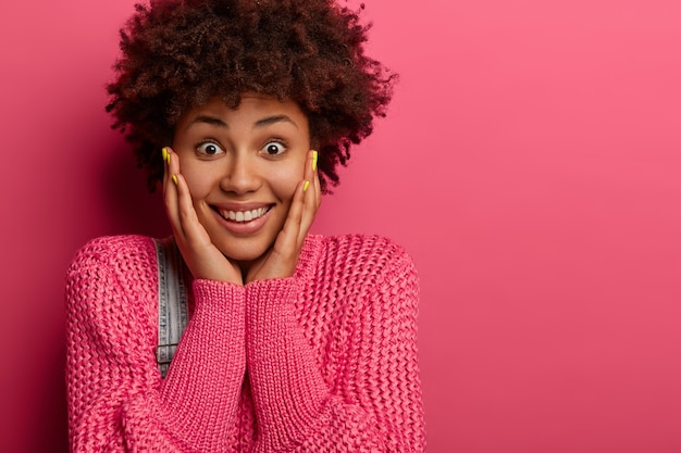 Portret van goed uitziende blije vrouw met afro kapsel close-up, houdt de handen op de wangen