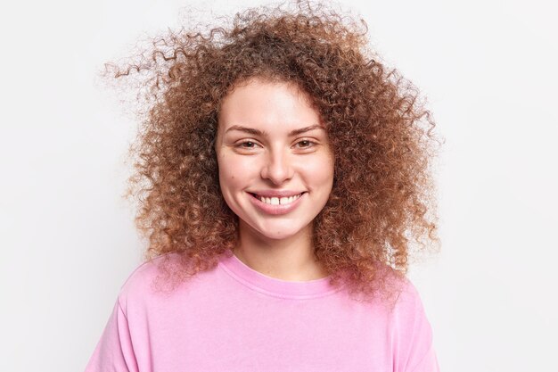 Portret van goed uitziende krullende vrouw glimlacht tandjes blij om te horen dat goed nieuws vrije tijd doorbrengt met vrienden gekleed in casual trui geïsoleerd over witte muur. Mensen en emoties concept