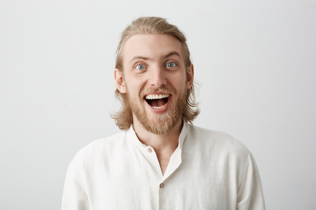 portret van grappige knappe bebaarde man met blond haar gezichten maken alsof hij gek doet