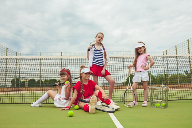 Portret van groep meisjes als tennisspelers die tennisracket houden tegen groen gras van openluchthof