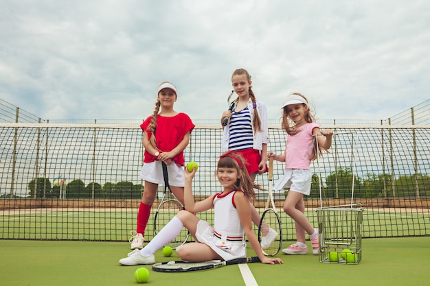 Gratis foto portret van groep meisjes als tennisspelers die tennisracket houden tegen groen gras van openluchthof