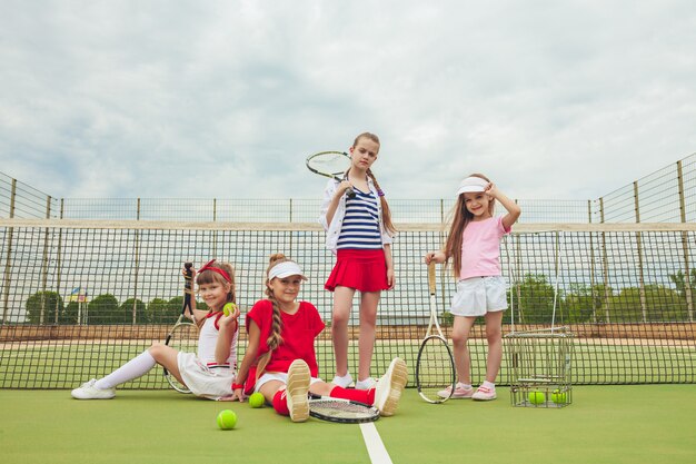 Portret van groep meisjes als tennisspelers die tennisrackets houden tegen groen gras van openluchthof.